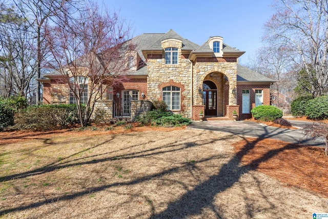 french country style house featuring stone siding, brick siding, and a front lawn