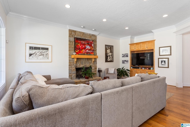 living room with a fireplace, recessed lighting, light wood-style floors, ornamental molding, and a textured ceiling