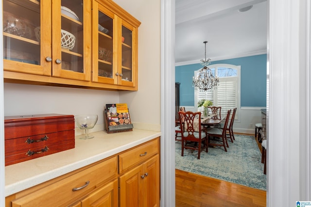 kitchen featuring glass insert cabinets, ornamental molding, wood finished floors, hanging light fixtures, and light countertops