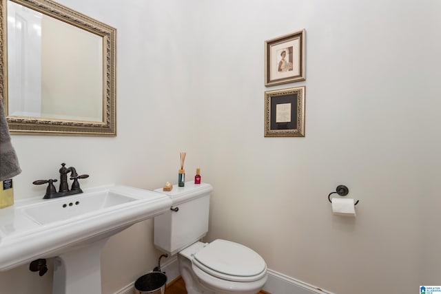 half bath with toilet, baseboards, and a sink