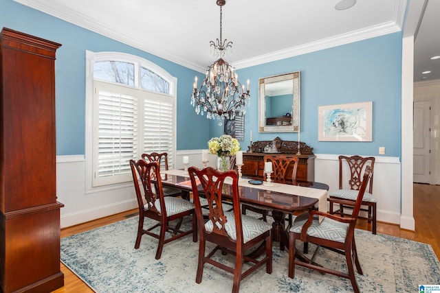 dining area featuring light wood-type flooring, ornamental molding, wainscoting, and an inviting chandelier