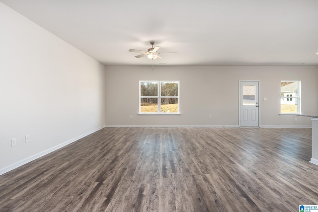 unfurnished living room featuring baseboards, ceiling fan, dark wood finished floors, and a healthy amount of sunlight