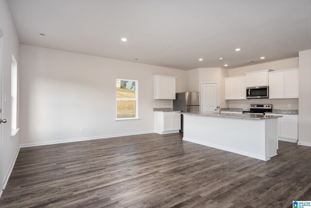 kitchen featuring dark wood-style flooring, stainless steel appliances, white cabinets, an island with sink, and light stone countertops