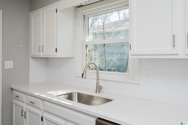 kitchen with light countertops, tasteful backsplash, a sink, and white cabinets