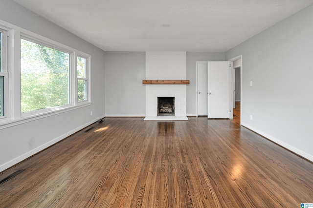 unfurnished living room featuring a brick fireplace, visible vents, dark wood finished floors, and baseboards