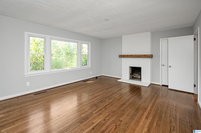 unfurnished living room featuring a fireplace, visible vents, dark wood-type flooring, a textured ceiling, and baseboards