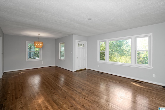 unfurnished living room featuring a textured ceiling, a chandelier, dark wood-style flooring, visible vents, and baseboards