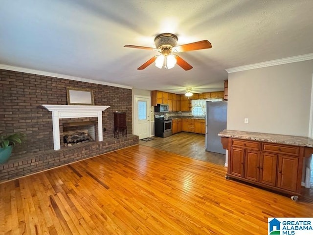 unfurnished living room featuring a fireplace, light wood-style flooring, ornamental molding, ceiling fan, and brick wall