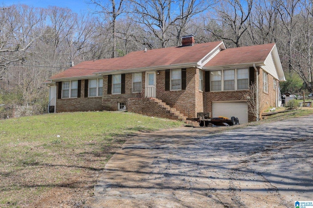 ranch-style house featuring brick siding, a front yard, a chimney, driveway, and an attached garage