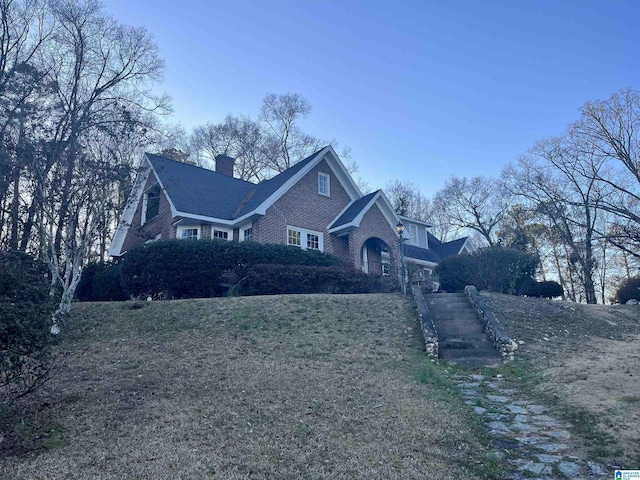 view of front of property featuring brick siding, a chimney, and a front yard