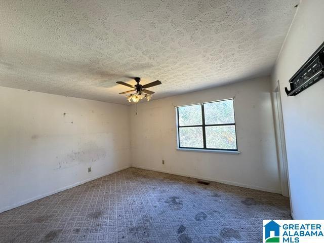 carpeted empty room featuring a ceiling fan, visible vents, a textured ceiling, and baseboards