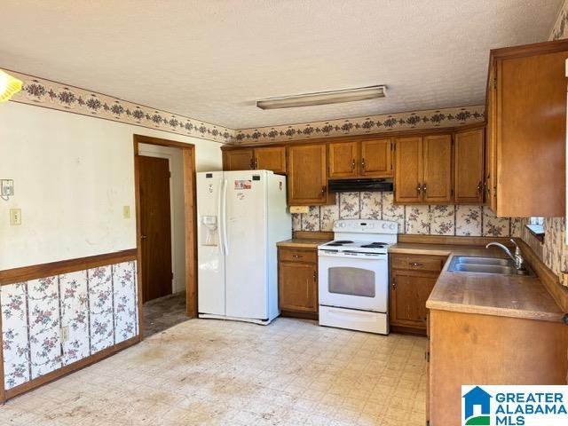 kitchen with light floors, brown cabinetry, a sink, white appliances, and under cabinet range hood