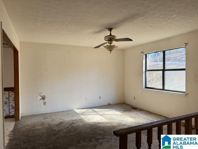 carpeted spare room with baseboards, a ceiling fan, and a textured ceiling