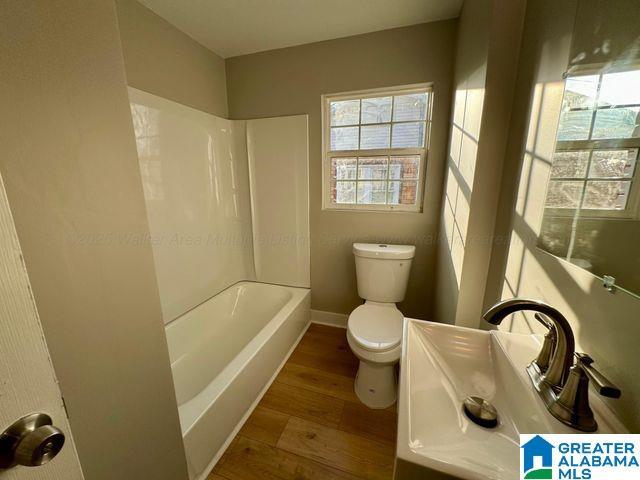 full bath featuring baseboards, toilet, wood finished floors, tub / shower combination, and a sink