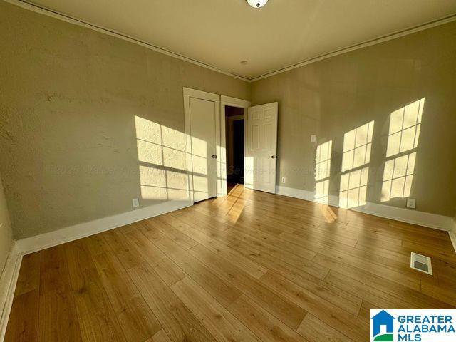 spare room with baseboards, wood finished floors, visible vents, and crown molding