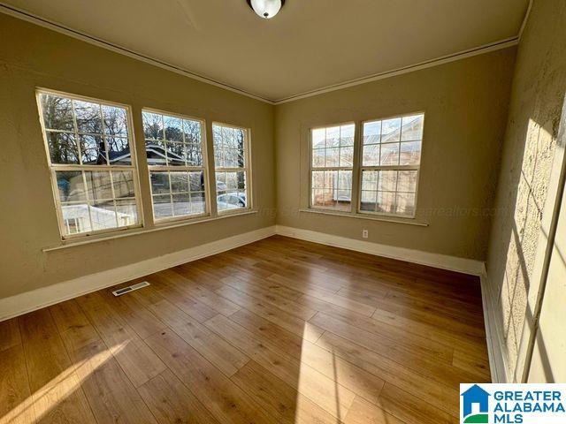 unfurnished room featuring visible vents, crown molding, baseboards, and wood finished floors