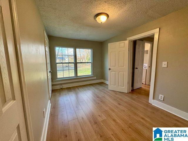 unfurnished bedroom featuring light wood-style floors, baseboards, and a textured ceiling