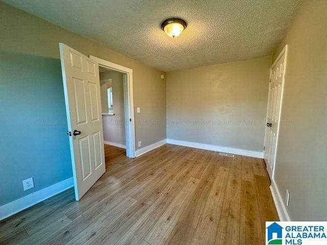 unfurnished room with a textured ceiling, light wood-type flooring, visible vents, and baseboards