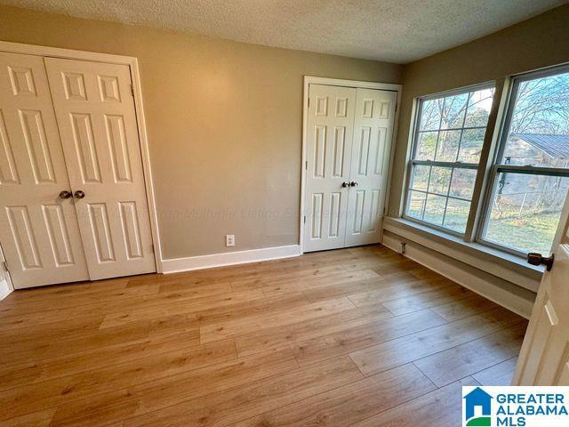 unfurnished bedroom with multiple closets, light wood-style flooring, baseboards, and a textured ceiling