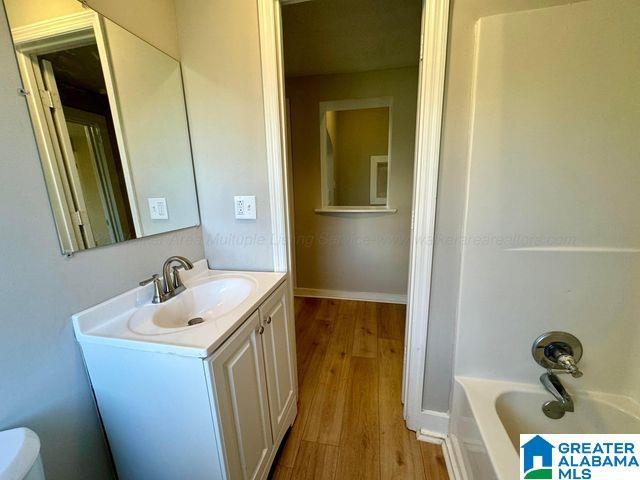 full bathroom featuring toilet, shower / bath combination, wood finished floors, vanity, and baseboards