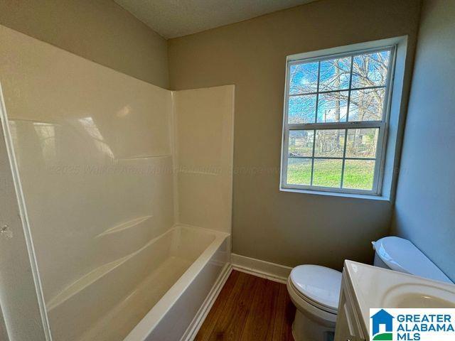 full bath with shower / washtub combination, toilet, vanity, wood finished floors, and baseboards