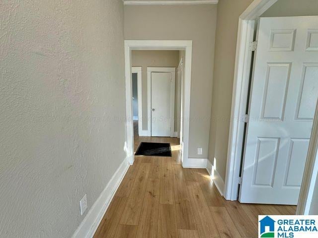 corridor featuring light wood-type flooring, a textured wall, and baseboards