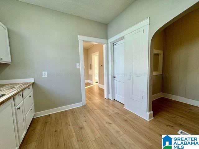 interior space with baseboards, arched walkways, white cabinets, light countertops, and light wood-type flooring