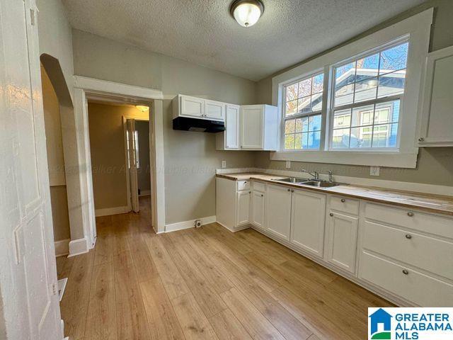 kitchen featuring light wood-style floors, light countertops, under cabinet range hood, white cabinetry, and a sink