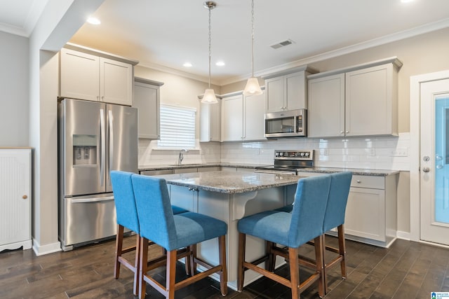 kitchen featuring dark wood-style flooring, stainless steel appliances, visible vents, ornamental molding, and a kitchen breakfast bar