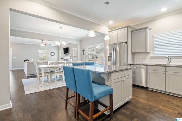 kitchen with appliances with stainless steel finishes, ornamental molding, open floor plan, a sink, and plenty of natural light