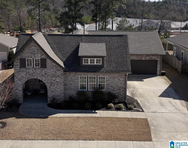 view of front of home featuring driveway, brick siding, a shingled roof, and fence