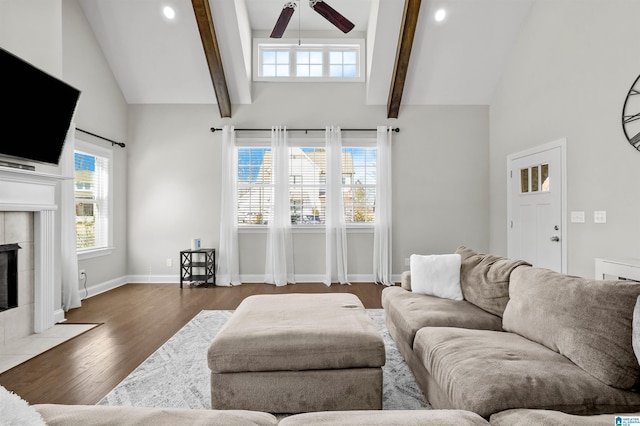 living room featuring dark wood-style flooring, a ceiling fan, baseboards, beamed ceiling, and a tiled fireplace