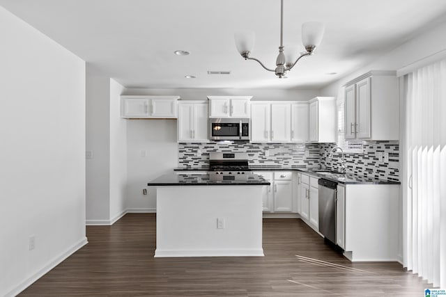 kitchen with appliances with stainless steel finishes, dark countertops, white cabinetry, and a center island