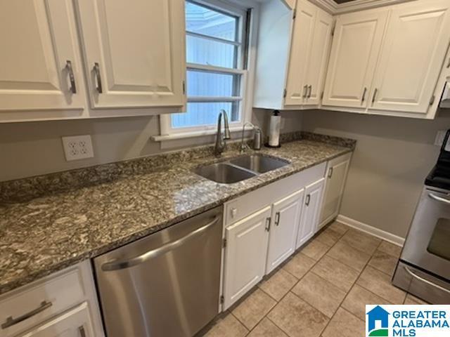 kitchen featuring range, dark stone countertops, stainless steel dishwasher, white cabinetry, and a sink