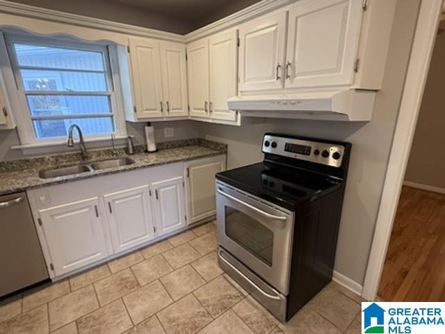 kitchen featuring under cabinet range hood, a sink, white cabinetry, appliances with stainless steel finishes, and light stone countertops