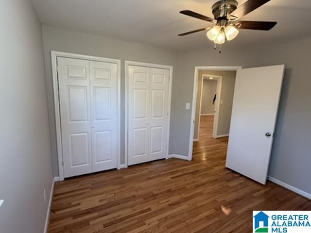 unfurnished bedroom featuring a ceiling fan, baseboards, dark wood-type flooring, and multiple closets