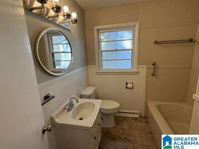 full bath featuring a baseboard radiator, toilet, a bathing tub, vanity, and wainscoting