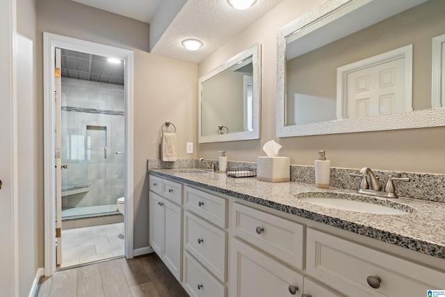 full bathroom featuring double vanity, a sink, a shower stall, a textured ceiling, and wood finished floors