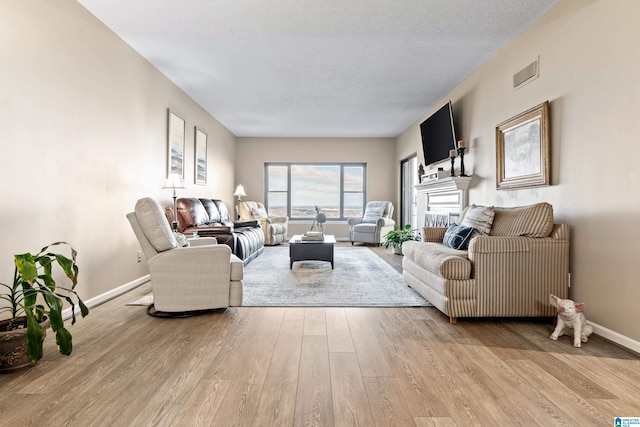 living area with light wood-type flooring, visible vents, a textured ceiling, and baseboards