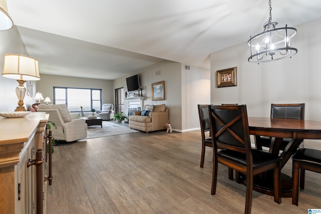 dining room with baseboards, visible vents, wood finished floors, a fireplace, and a notable chandelier