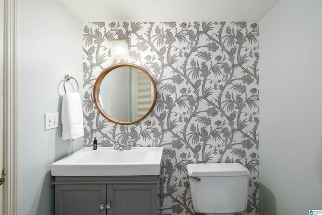 half bathroom with toilet, wallpapered walls, and vanity