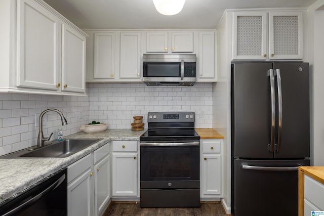 kitchen featuring dark wood finished floors, stainless steel appliances, decorative backsplash, white cabinetry, and a sink