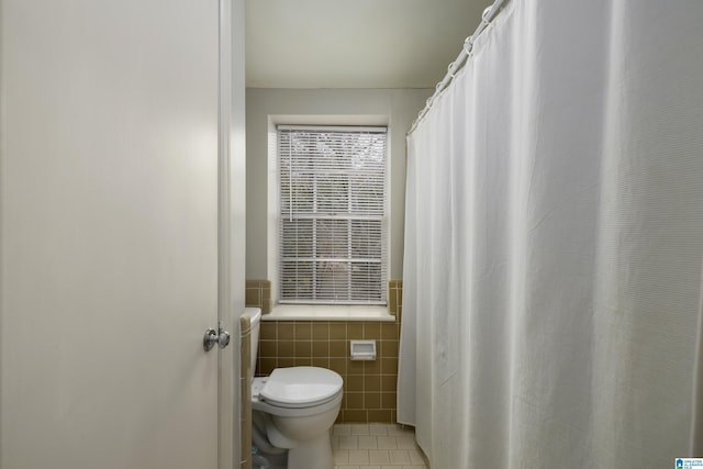 bathroom with toilet, a wainscoted wall, tile patterned flooring, and tile walls