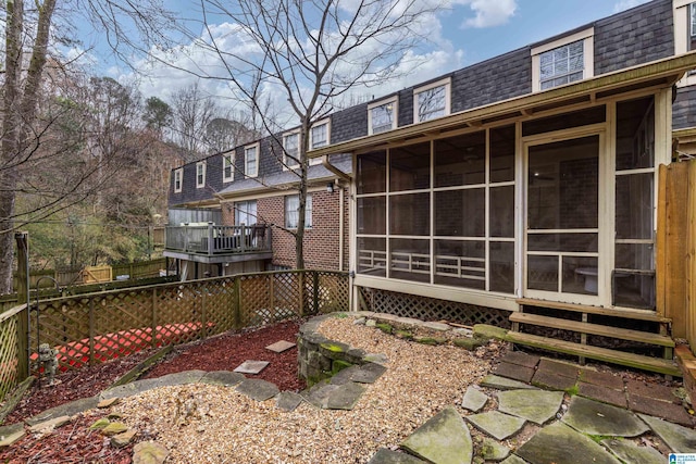 back of house featuring a shingled roof, a sunroom, fence, and mansard roof