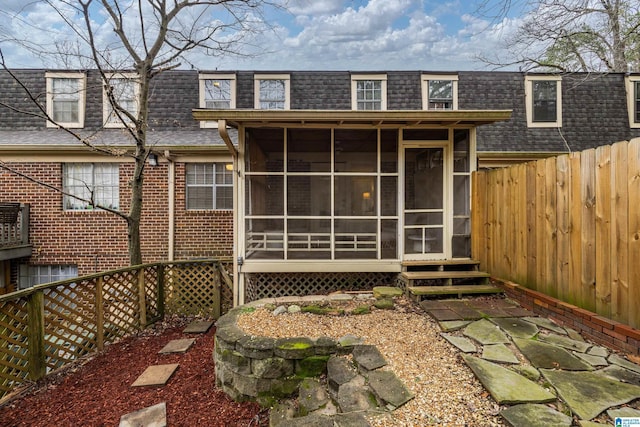 back of property featuring a sunroom, a fenced backyard, mansard roof, and brick siding