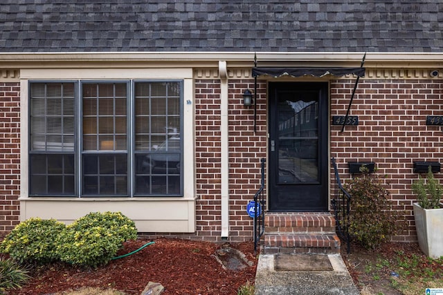 property entrance with brick siding, roof with shingles, and mansard roof