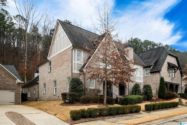 tudor house featuring roof with shingles, brick siding, a chimney, and board and batten siding