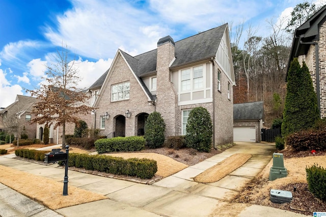 english style home with a shingled roof, a chimney, and brick siding