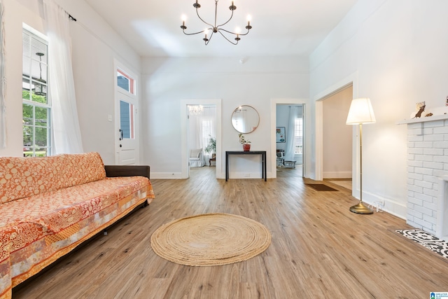 living area with light wood finished floors, baseboards, a brick fireplace, and a chandelier