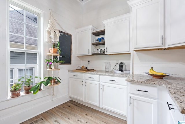 kitchen with light wood-style floors, white cabinets, light stone counters, and open shelves